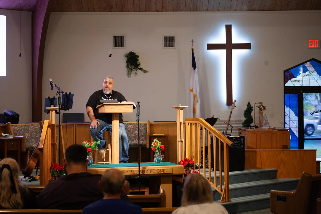 Pastor Damien teaching beside the illuminated cross at The Way